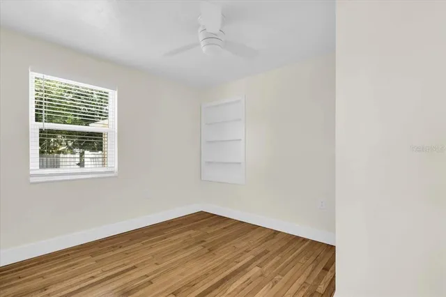 a view of empty room with wooden floor and fan
