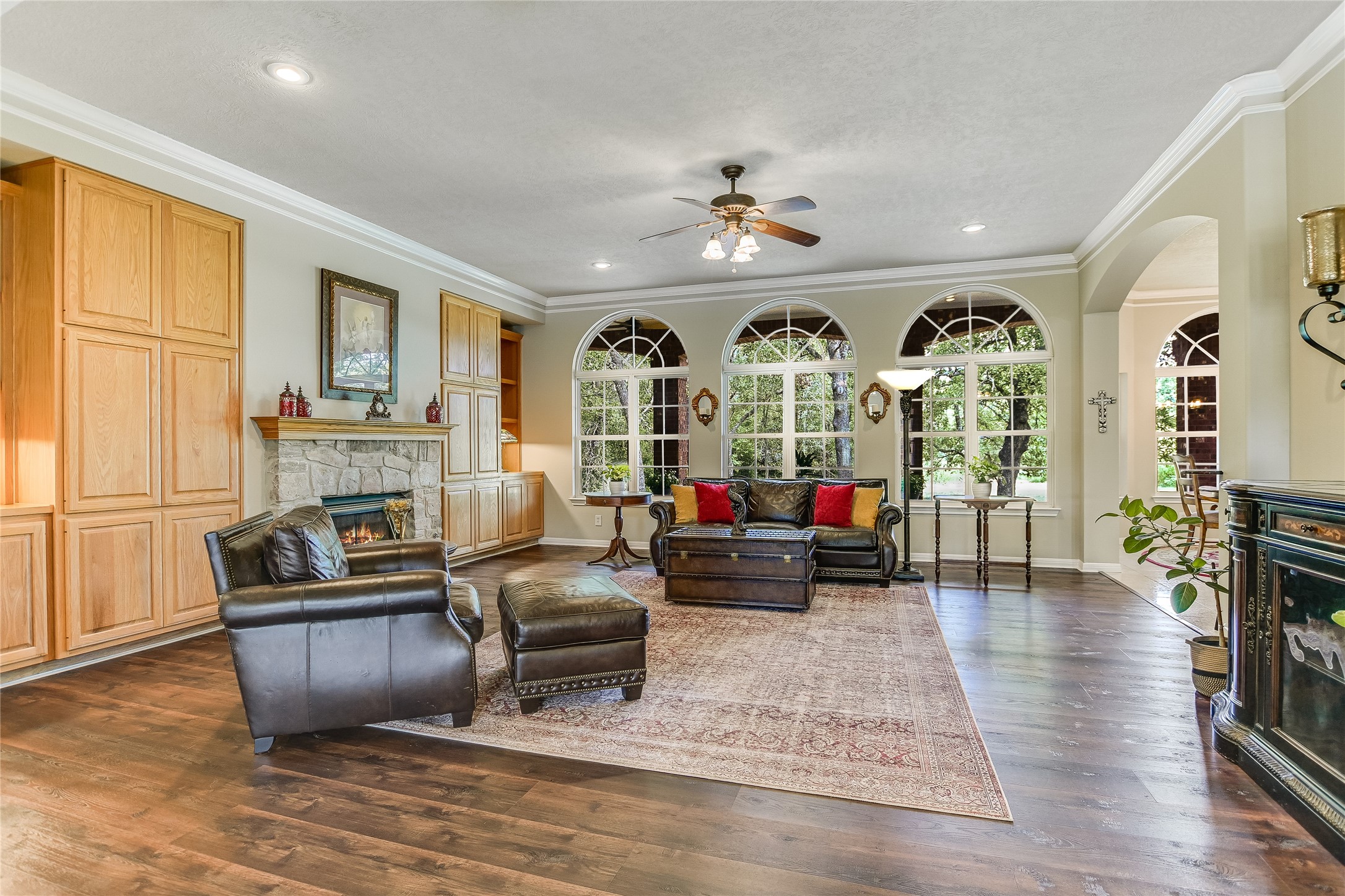 741 Knobbs Road McDade, TX 78650 - Photo 6 of 38 Natural light floods this inviting living room through multiple arched windows, complementing the warm wood flooring and stone fireplace.