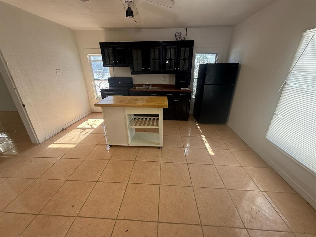 304 Neblett Street Eastland, TX 76448 - Photo 5 of 15 Kitchen with dark cabinets, black appliances, a ceiling fan, light tile patterned floors, and glass insert cabinets
