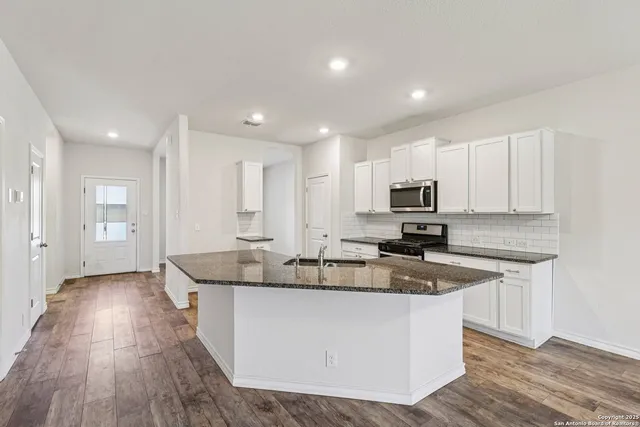 a kitchen with stainless steel appliances granite countertop a sink a stove a refrigerator and white cabinets