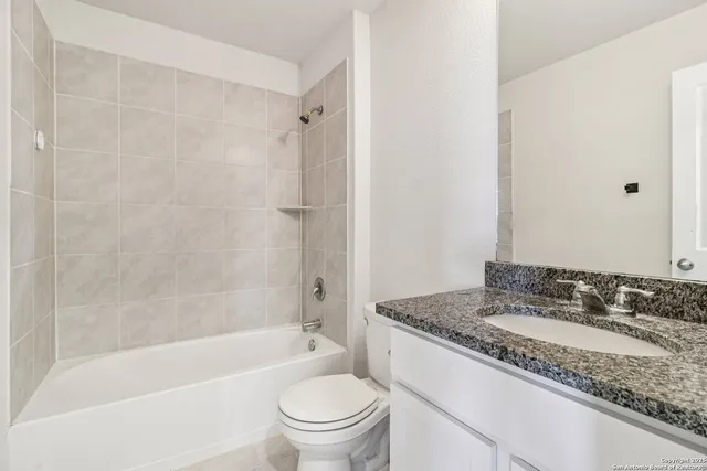 a bathroom with a granite countertop bathtub shower sink vanity mirror and toilet