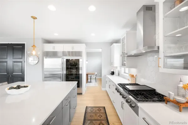 a kitchen with stainless steel appliances a stove a sink a refrigerator white cabinets and wooden floor