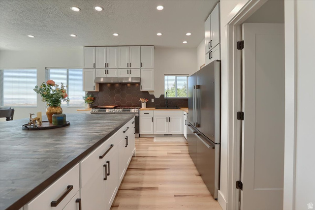 828 South Deer Road Tooele, UT 84074 - Photo 10 of 51 Spacious kitchen featuring an expansive center island with ample storage, light wood-finish flooring, white cabinetry with dark hardware, a hexagonal tile backsplash, and recessed lighting throughout