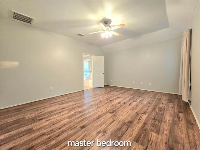 an empty room with wooden floor chandelier fan and windows