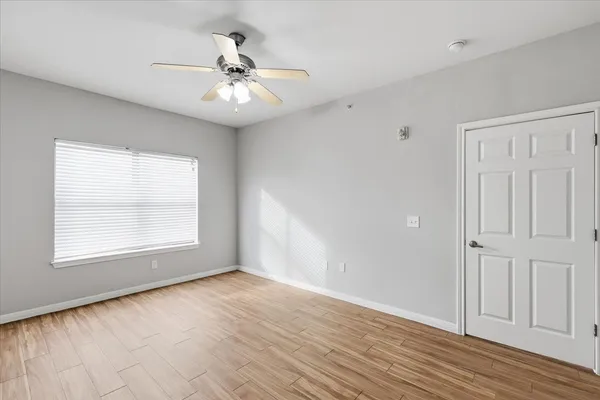 an empty room with wooden floor chandelier fan and windows