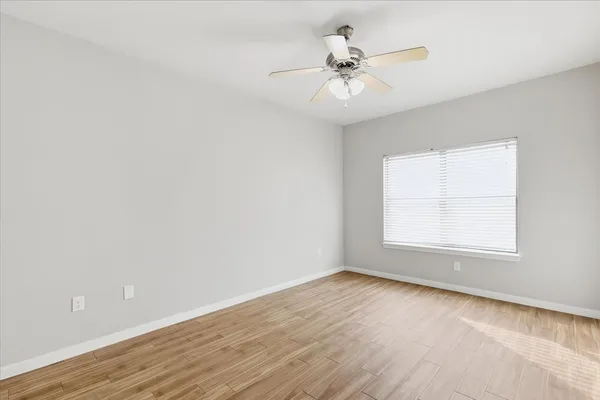an empty room with wooden floor fan and windows