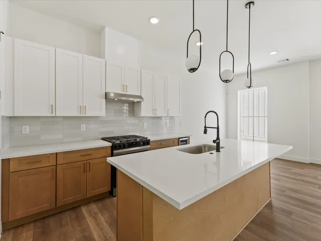 a view of an empty room and kitchen with wooden floor