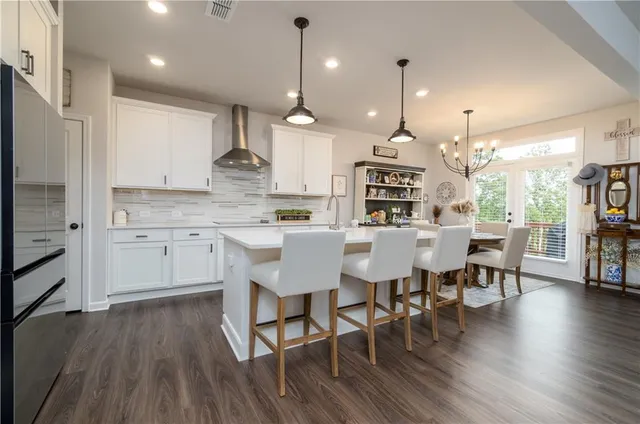 a kitchen with stainless steel appliances kitchen island granite countertop a stove a refrigerator a kitchen island a dining table and chairs with wooden floor