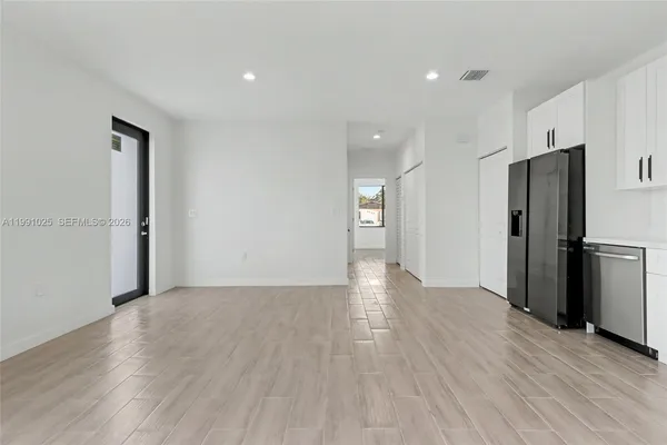 a view of an empty room with wooden floor and a kitchen