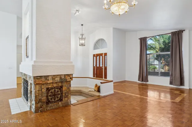 a view of an empty room with chandelier fan and wooden floor