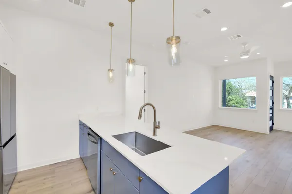 a kitchen with stainless steel appliances a stove a sink a refrigerator a center island a stove and white cabinets with wooden floor