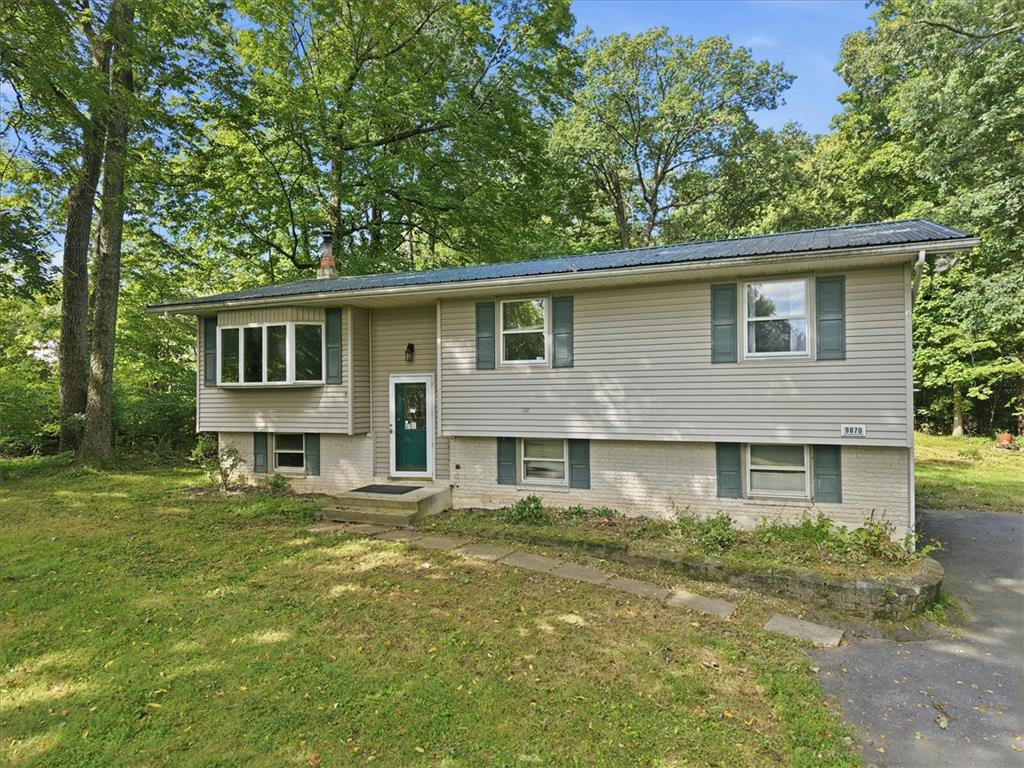 Mature trees frame a classic split-level home featuring vinyl siding and a metal roof.