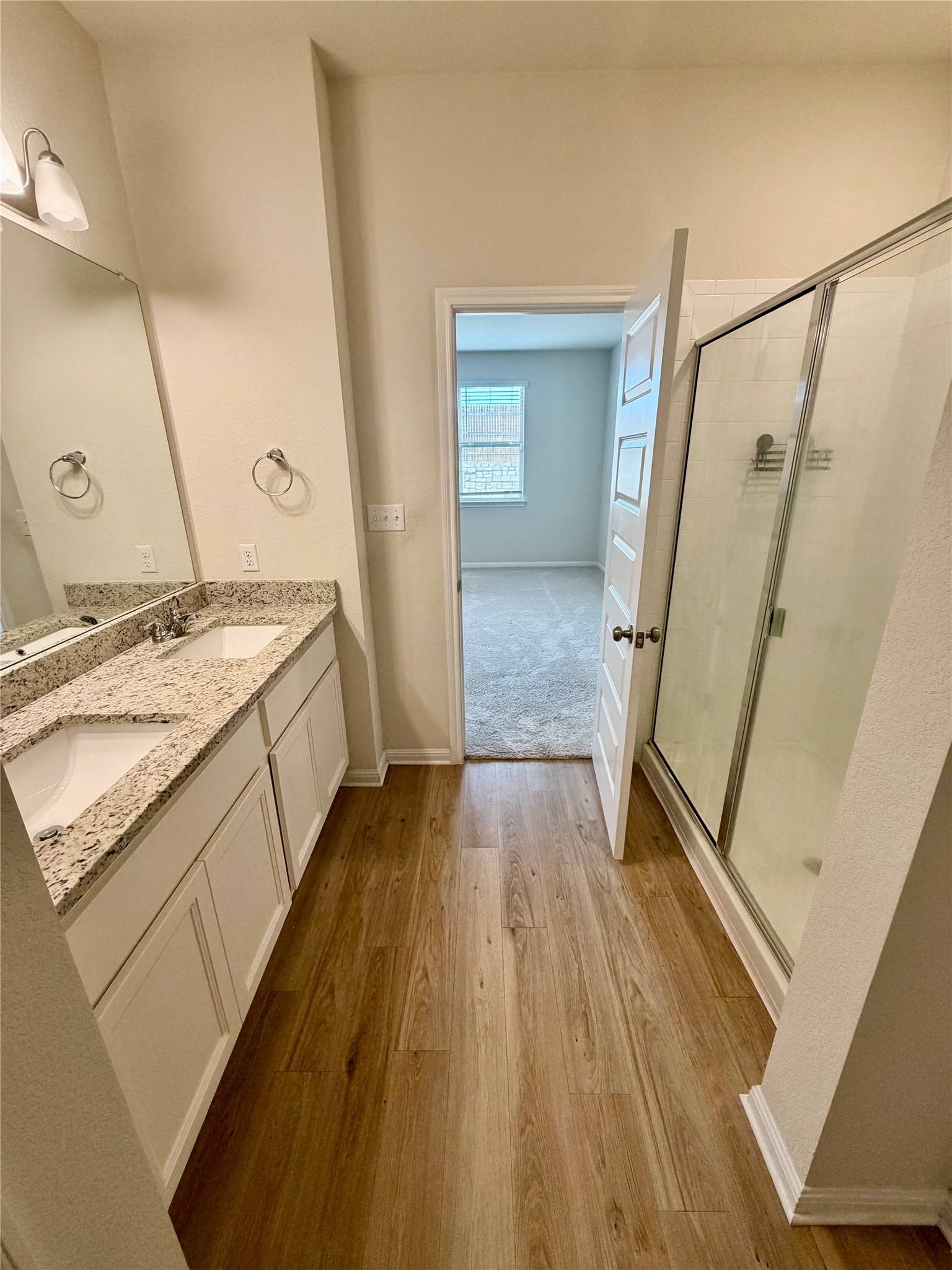 305 Tolo Drive Elgin, TX 78621 - Photo 16 of 27 Bathroom featuring wood-finish flooring, a double vanity with granite countertops, and a glass-enclosed shower