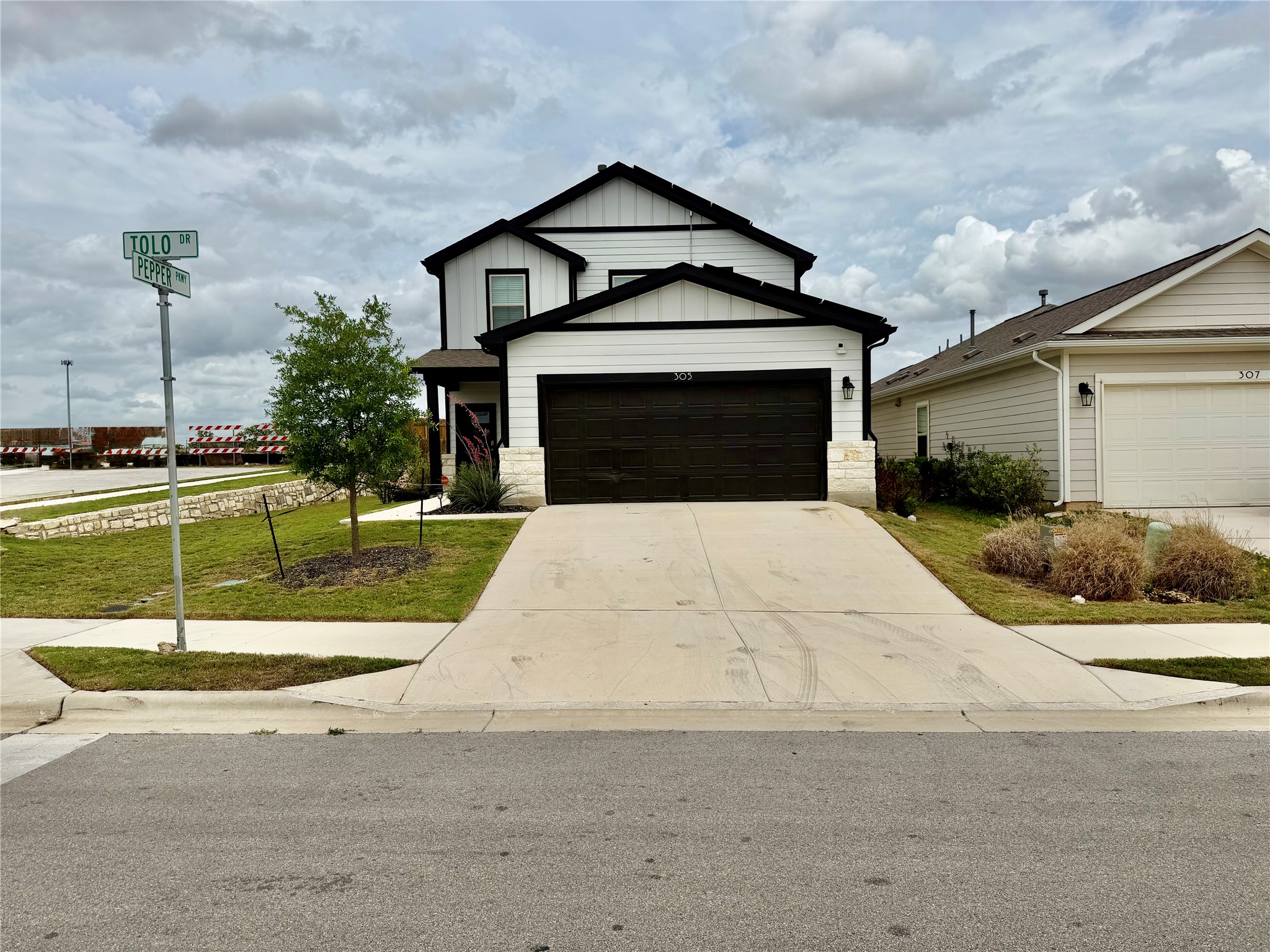 305 Tolo Drive Elgin, TX 78621 - Photo 2 of 27 Contemporary two-story residence featuring a white vertical siding exterior with black trim, an attached two-car garage with a dark door, a concrete driveway, and a manicured lawn
