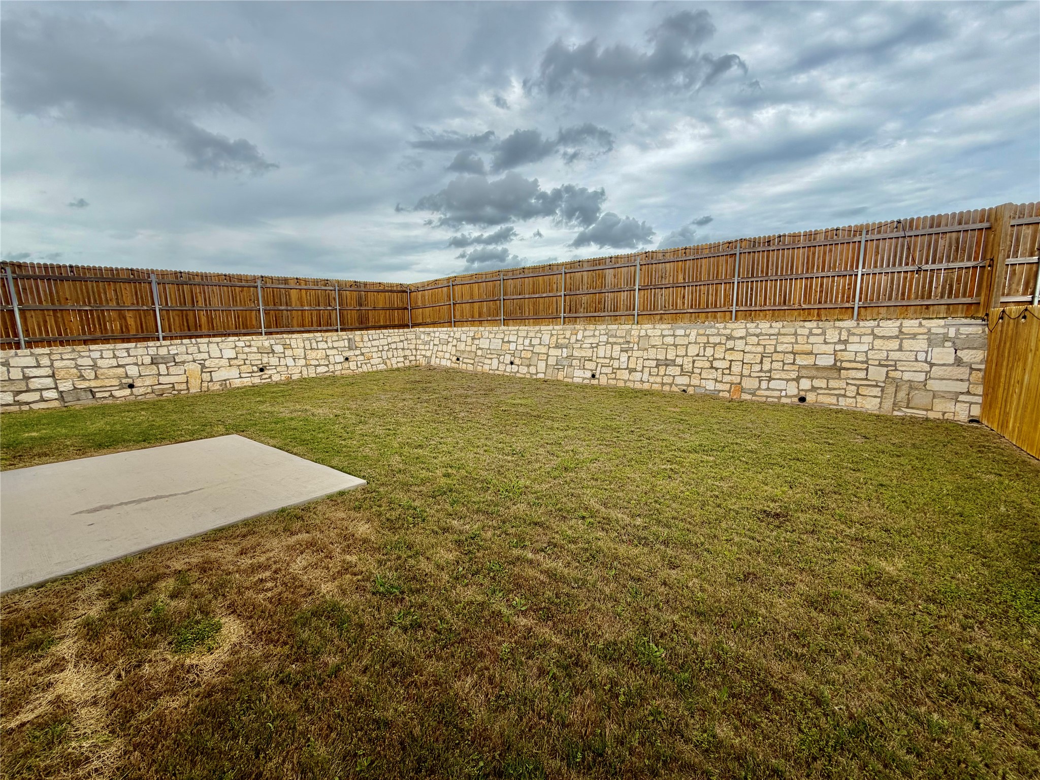 305 Tolo Drive Elgin, TX 78621 - Photo 25 of 27 Expansive backyard featuring a stone retaining wall, wood privacy fence, and a concrete patio slab
