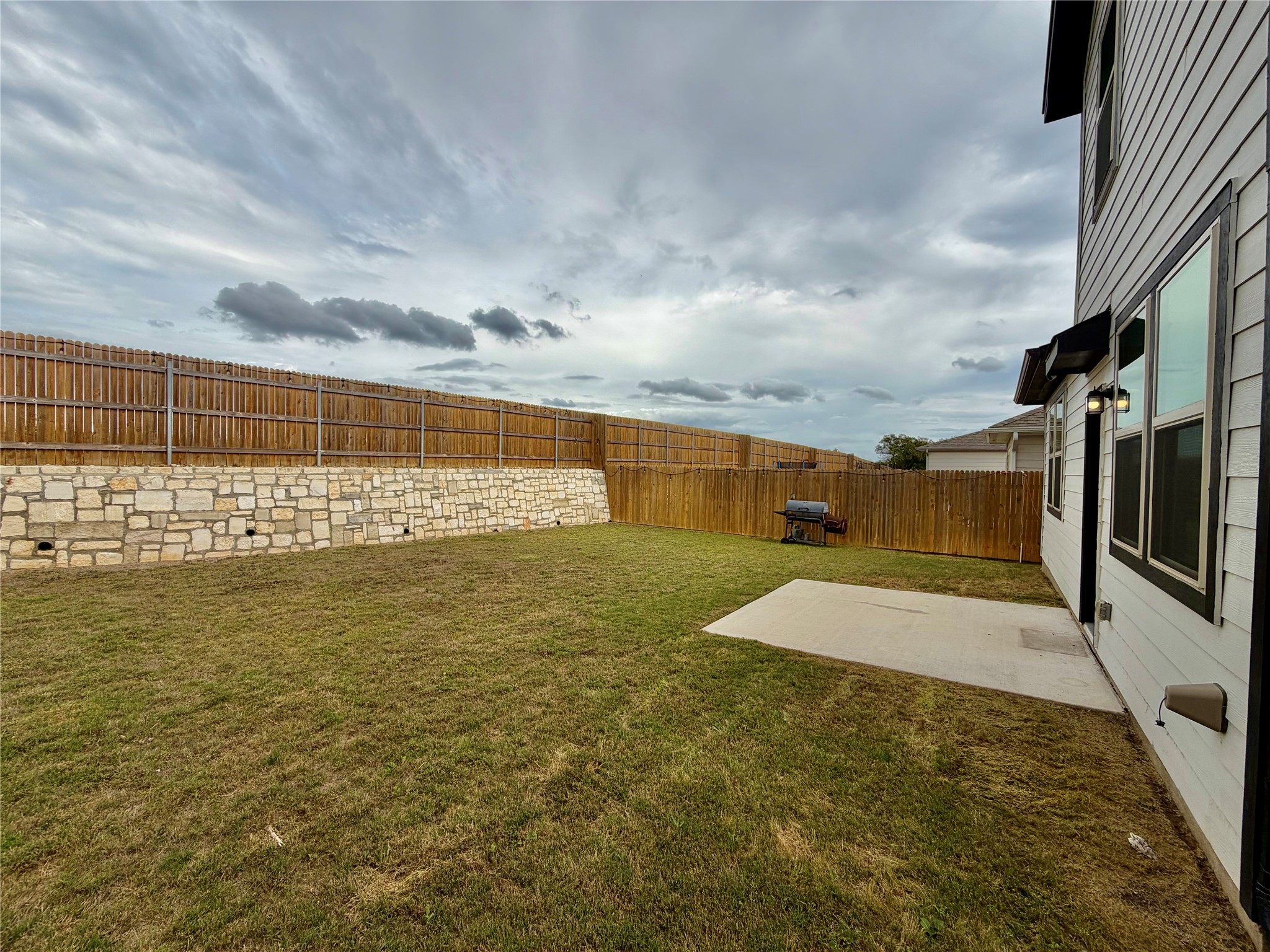 305 Tolo Drive Elgin, TX 78621 - Photo 26 of 27 Fenced backyard featuring a stone retaining wall, level lawn, and concrete patio