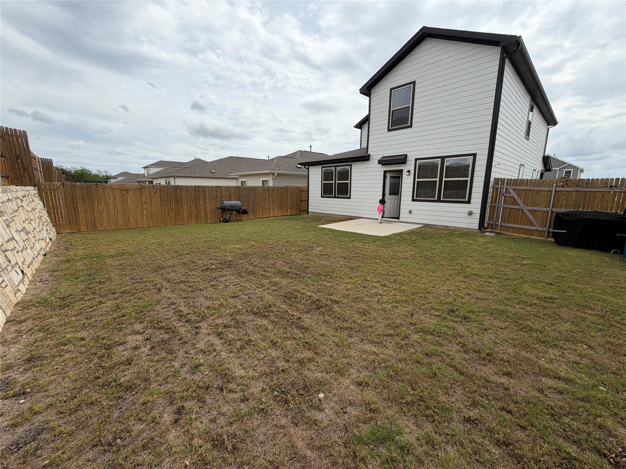 305 Tolo Drive Elgin, TX 78621 - Photo 27 of 27 Spacious backyard with a wood privacy fence, stone retaining wall, and a concrete patio