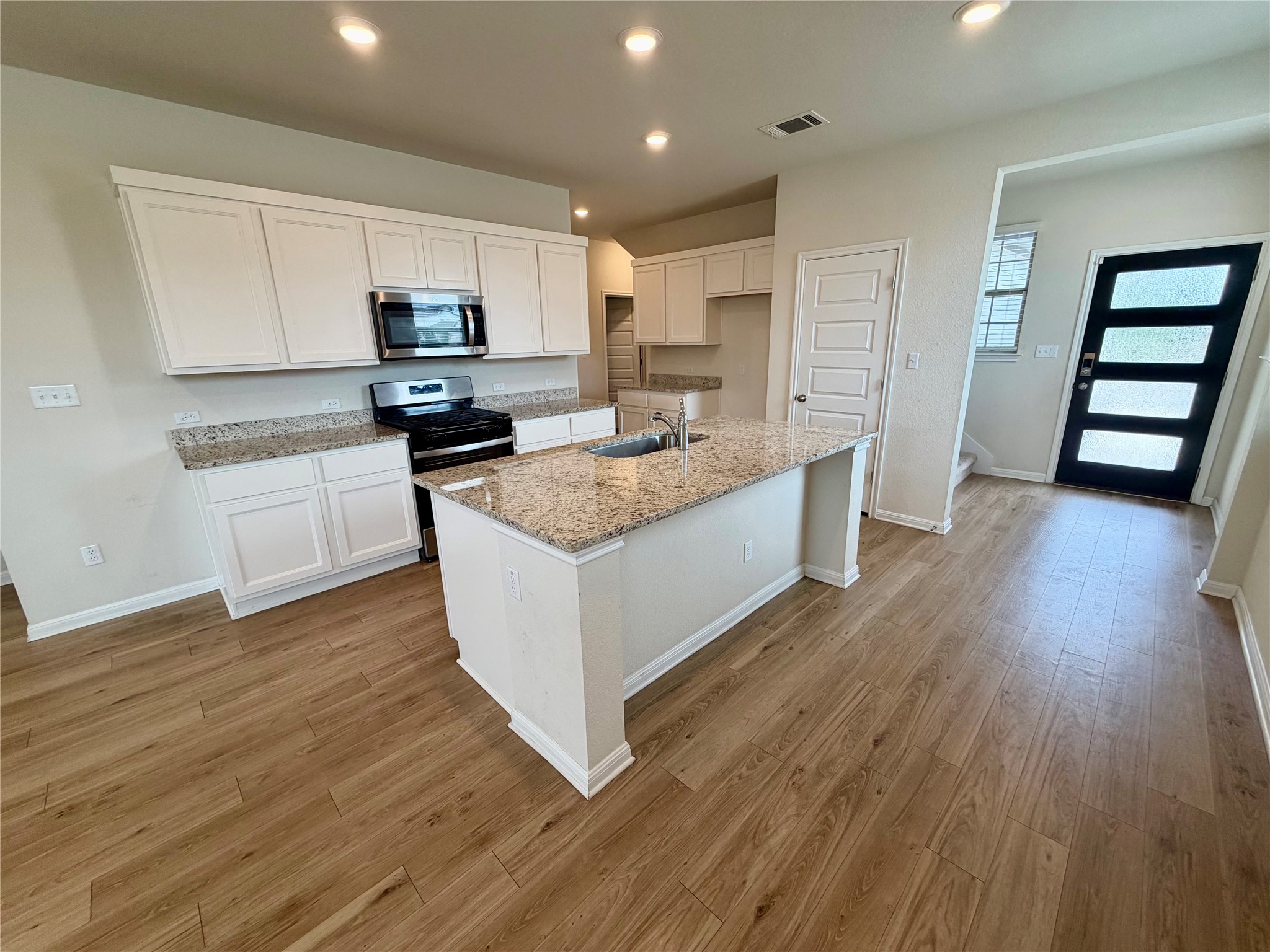 305 Tolo Drive Elgin, TX 78621 - Photo 5 of 27 Kitchen featuring white shaker cabinetry, granite countertops, stainless steel appliances, a central island with an undermount sink, and wood-finish flooring