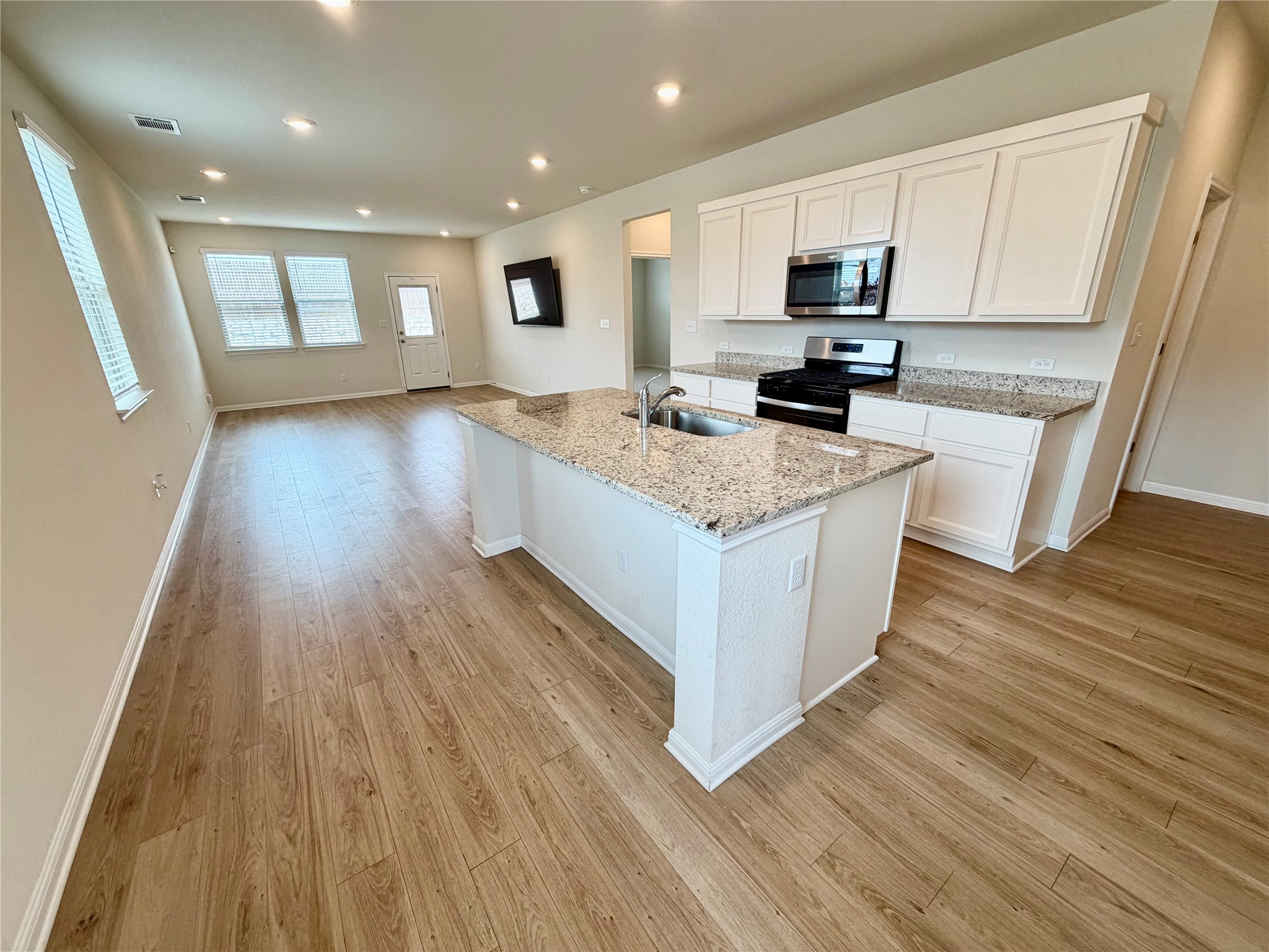 305 Tolo Drive Elgin, TX 78621 - Photo 6 of 27 Kitchen with central island featuring a stainless steel sink, granite countertops, wood-finish flooring, white cabinetry, and recessed lighting