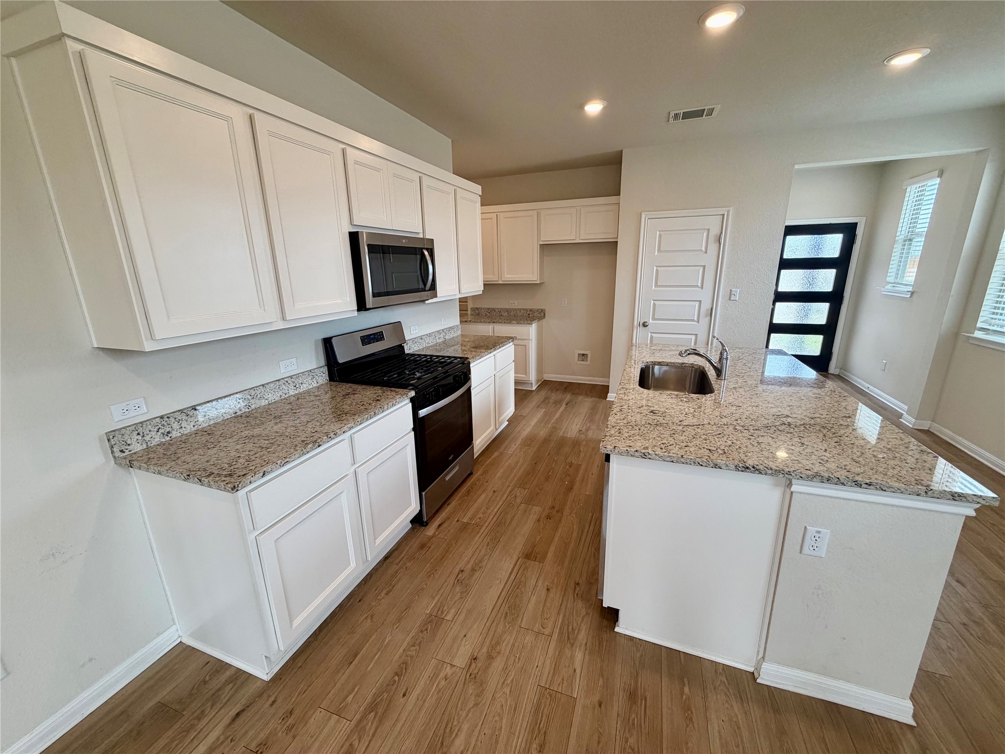 305 Tolo Drive Elgin, TX 78621 - Photo 7 of 27 Kitchen featuring wood-finish flooring, white cabinetry, granite countertops, stainless steel appliances, and an island with a built-in sink