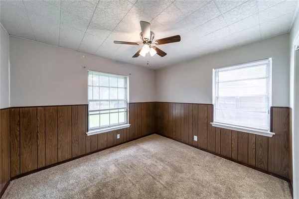 an empty room with chandelier fan and windows