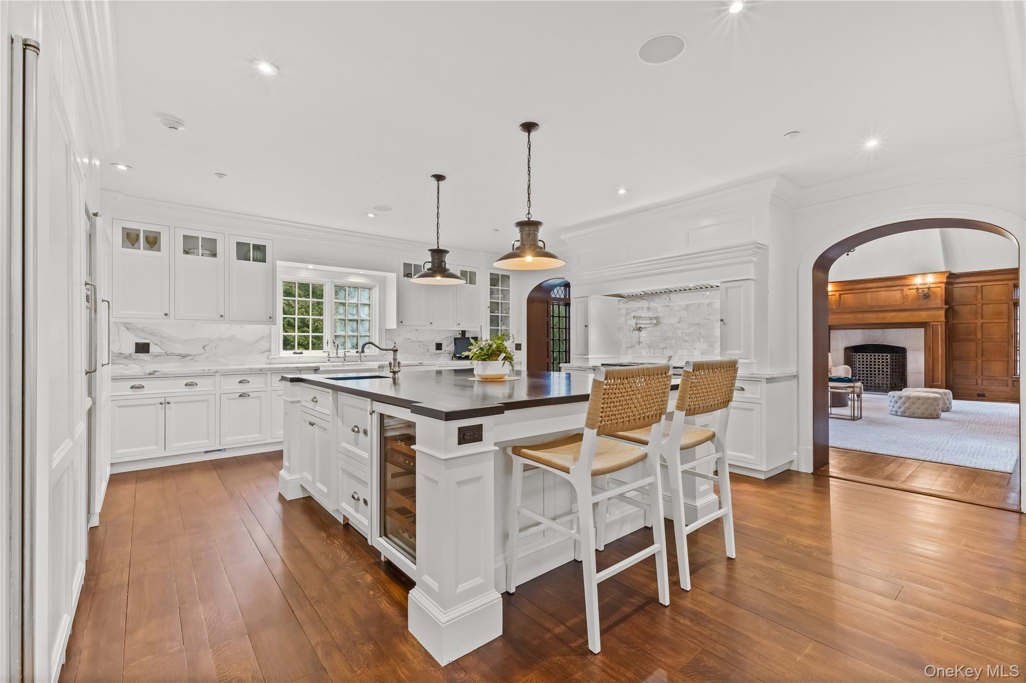19 Park Drive South Rye, NY 10580 - Photo 13 of 42 Bright, chef's kitchen featuring custom white cabinetry, marble backsplash, and a spacious center island with seating—perfect for entertaining and everyday living. Warm hardwood floors, elegant pendant lighting, and an open flow into the adjacent living space create a sophisticated yet inviting atmosphere.