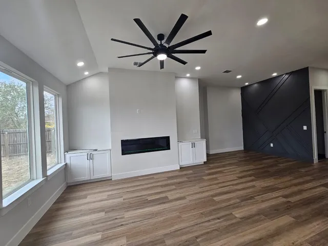 a view of an empty room with wooden floor and a kitchen
