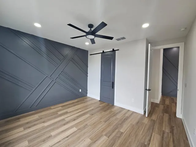an empty room with wooden floor fan and windows