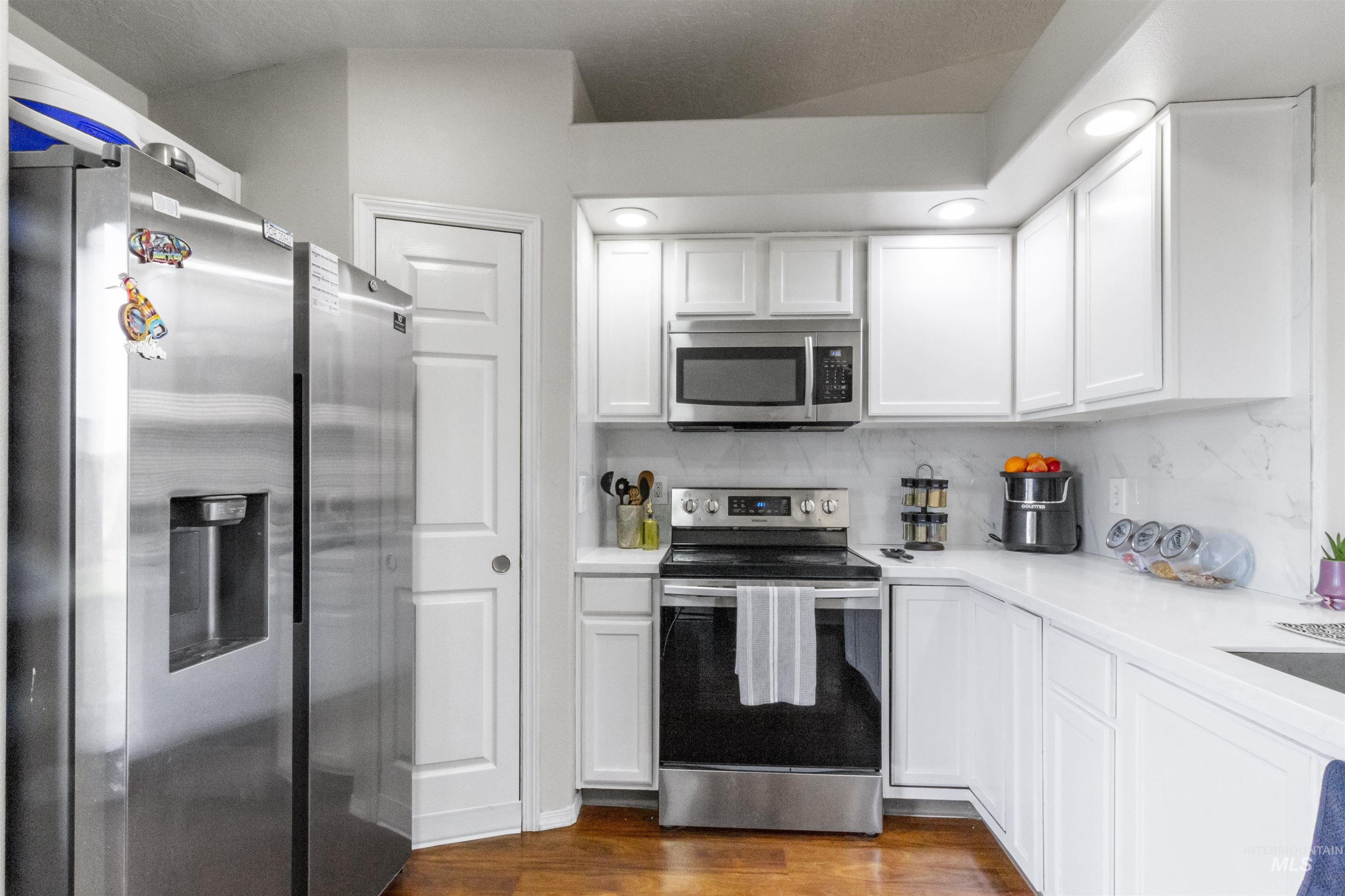 1823 Cambridge Street Caldwell, ID 83607 - Photo 5 of 10 Kitchen featuring stainless steel appliances, white cabinetry, dark wood finished floors, and tasteful backsplash