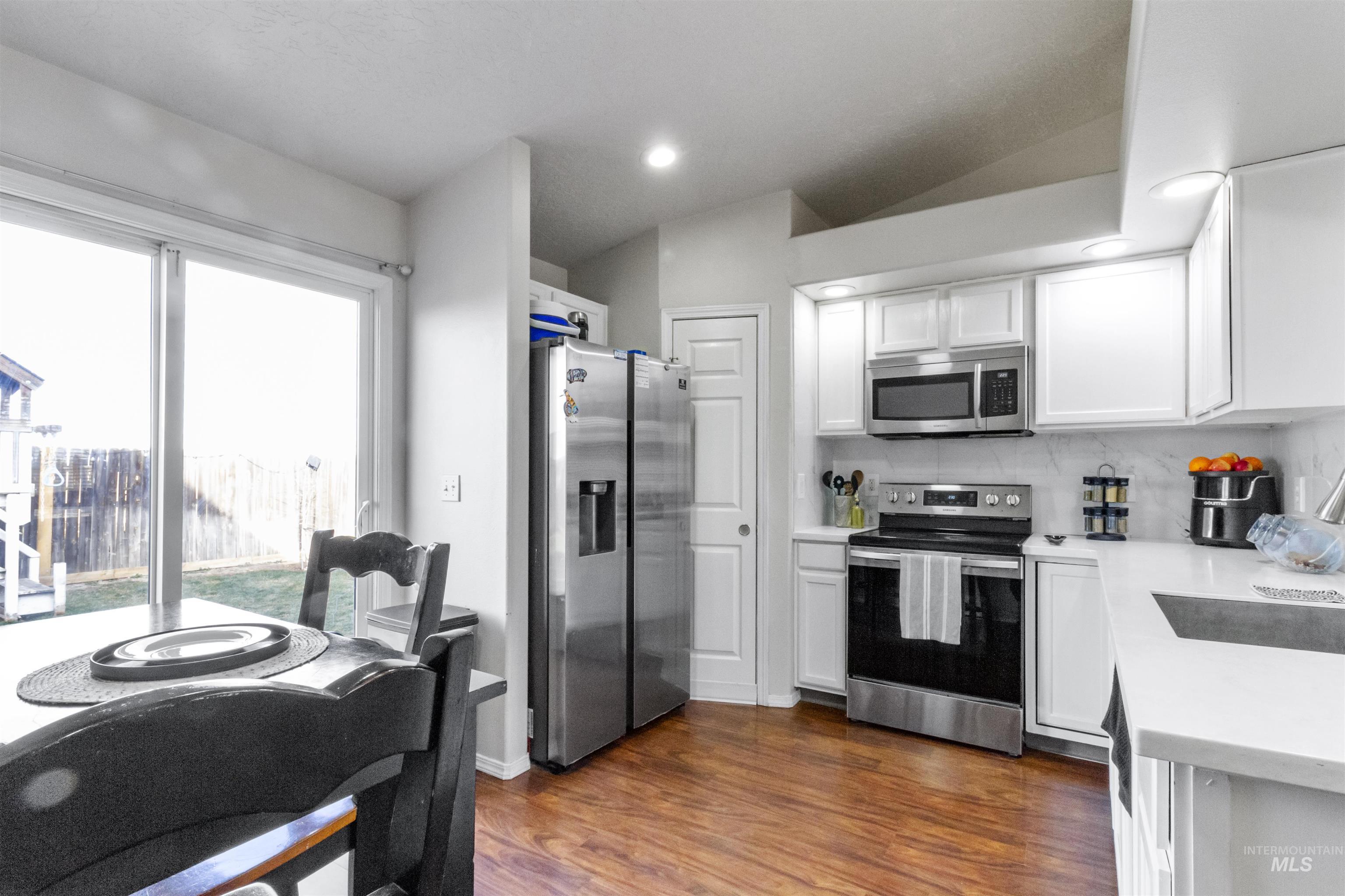 1823 Cambridge Street Caldwell, ID 83607 - Photo 7 of 10 Kitchen featuring stainless steel appliances, white cabinets, dark wood-style flooring, backsplash, and light stone counters