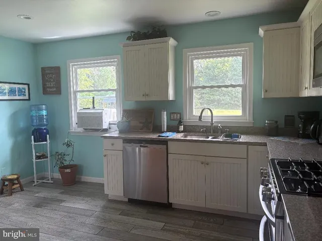 a kitchen with stainless steel appliances granite countertop a sink a stove a refrigerator white cabinets and wooden floor