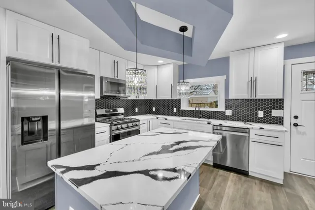 a kitchen with stainless steel appliances granite countertop a stove a sink dishwasher a refrigerator and white cabinets with wooden floor