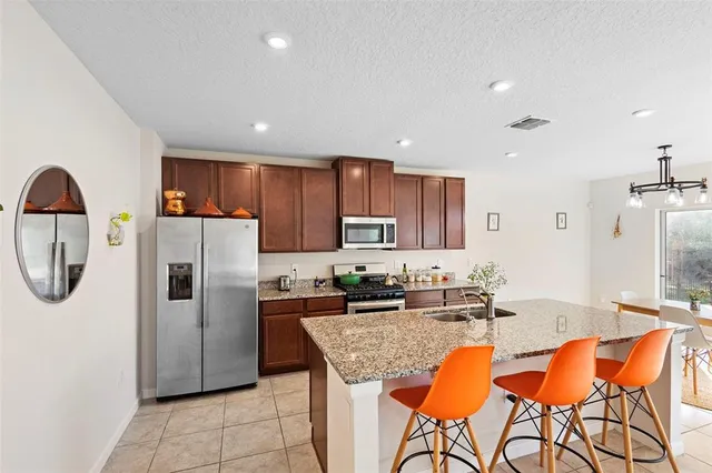 a kitchen with stainless steel appliances granite countertop a refrigerator a sink a stove a dining table and chairs