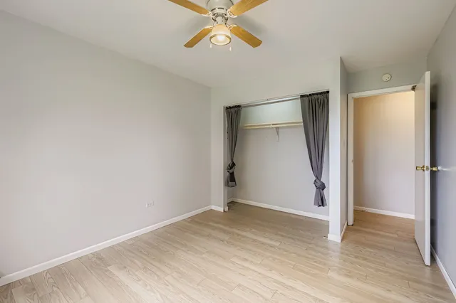 a view of an empty room with wooden floor and a ceiling fan