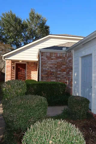 a view of a brick house with plants and large trees