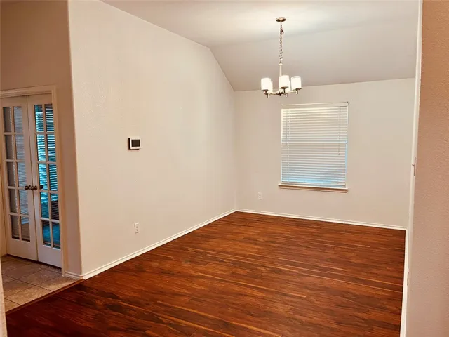 an empty room with wooden floor chandelier and windows