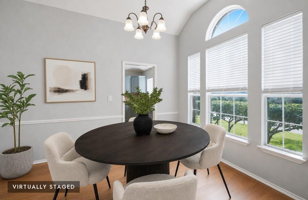 2074 Briarcliff Road Lewisville, TX 75067 - Photo 4 of 40 Dining area featuring vaulted ceilings, a decorative chandelier, multiple windows with blinds, an arched transom window, and wood-finish flooring - virtually staged