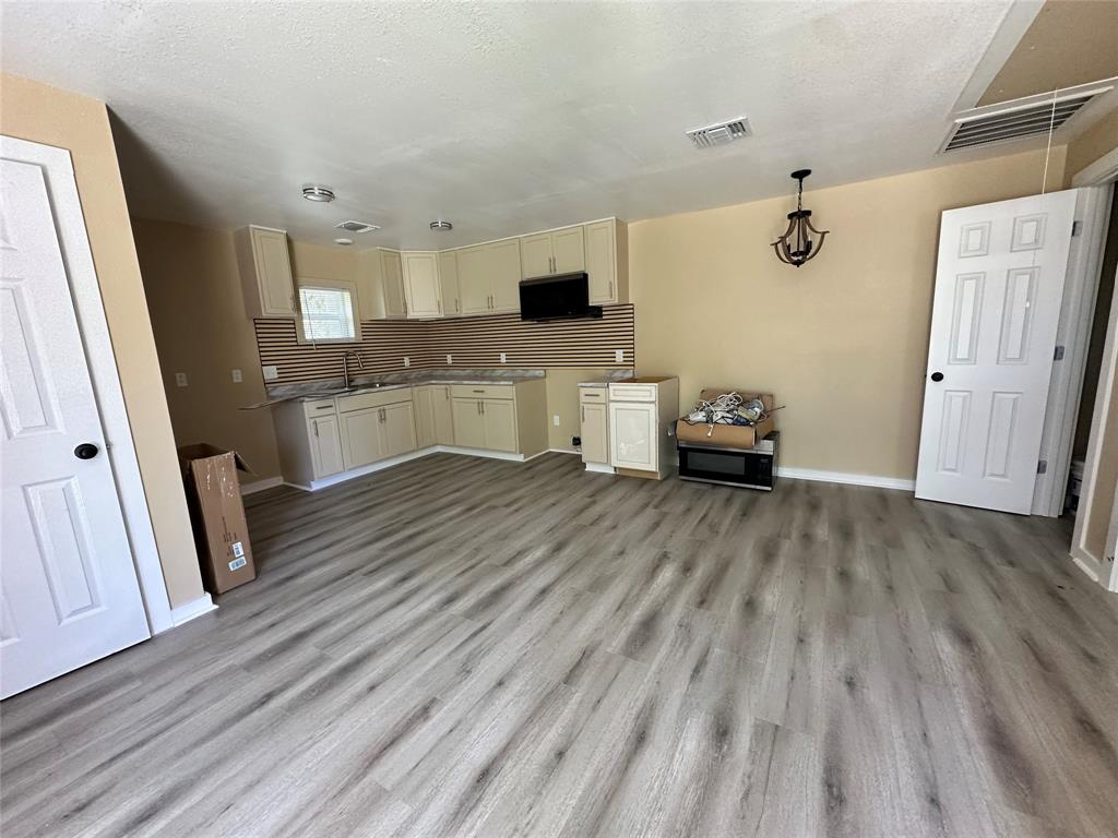 4101 North 19th Street Waco, TX 76708 - Photo 8 of 8 Kitchen and living room with light wood-style floors, decorative backsplash, a textured ceiling, pendant lighting, and open floor plan