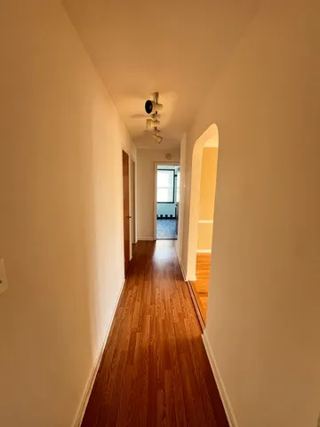 a view of a hallway with wooden floor and a bathroom