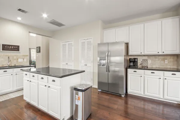 a kitchen with granite countertop a refrigerator a sink and white cabinets