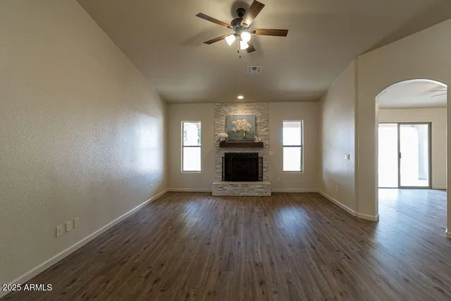 an empty room with wooden floor a ceiling fan a fireplace and windows
