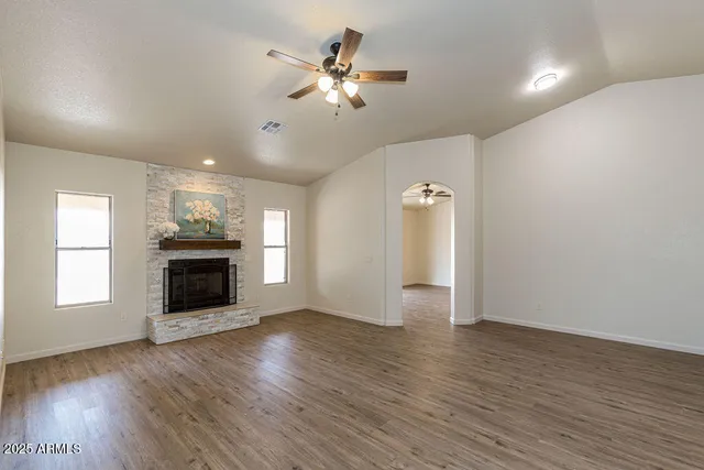 an empty room with wooden floor fireplace and windows