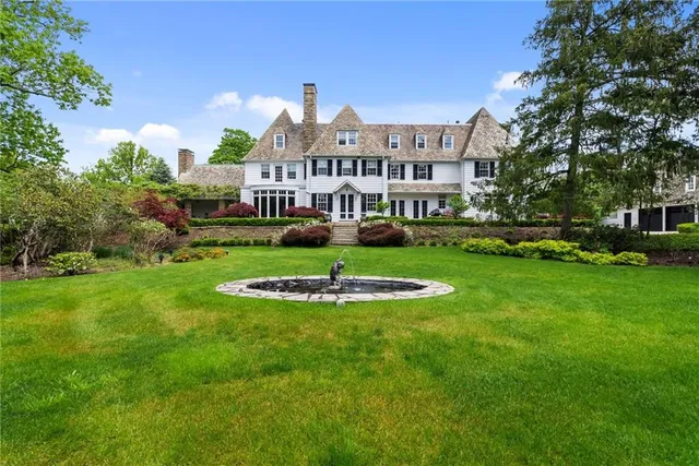 a view of a white house in front of a big yard with plants and large trees