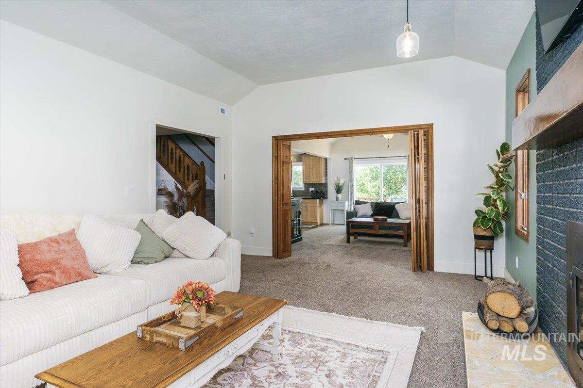1401 Chokecherry Drive Pocatello, ID 83204 - Photo 7 of 46 Living area featuring vaulted ceilings, carpet flooring, a stone-front fireplace with a wood mantle, and a doorway with accordion-style wood doors