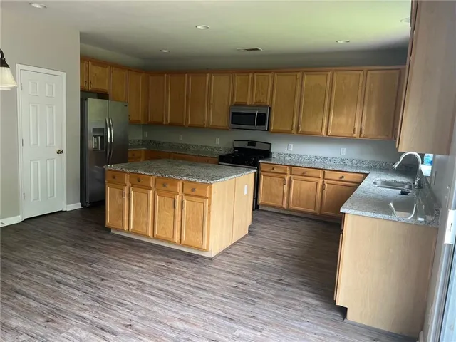 a kitchen with stainless steel appliances granite countertop a stove top oven a refrigerator a sink and dishwasher with wooden floor