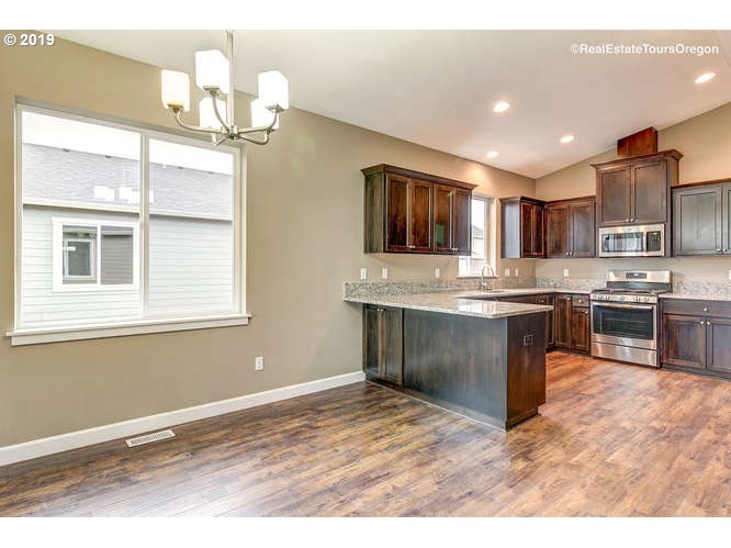 1060 6th Street Gervais, OR 97026 - Photo 15 of 30 a kitchen with kitchen island granite countertop a stove top oven a sink dishwasher a dining table and chairs with wooden floor