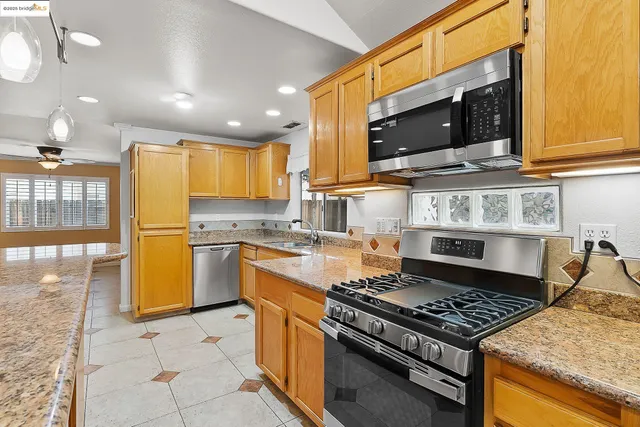 a kitchen with stainless steel appliances granite countertop a sink a stove a refrigerator and island with wooden floor