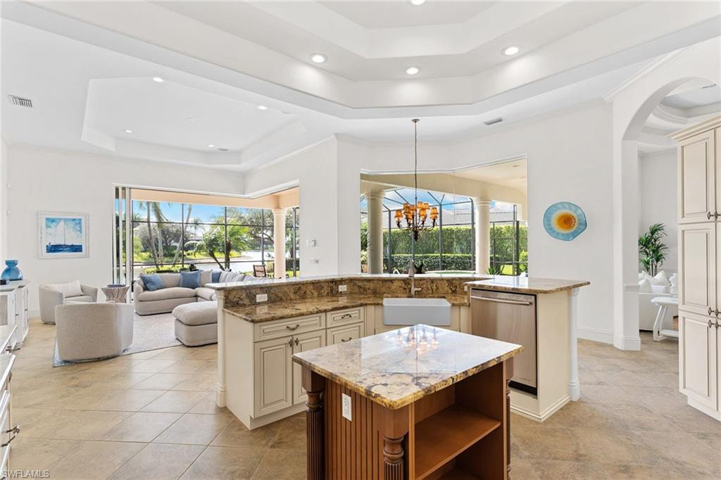 7506 Hogan Court Naples, FL 34113 - Photo 48 of 49 Dual tone kitchen with light stone counters, a tray ceiling, stainless steel dishwasher, open floor plan, and suspended lighting