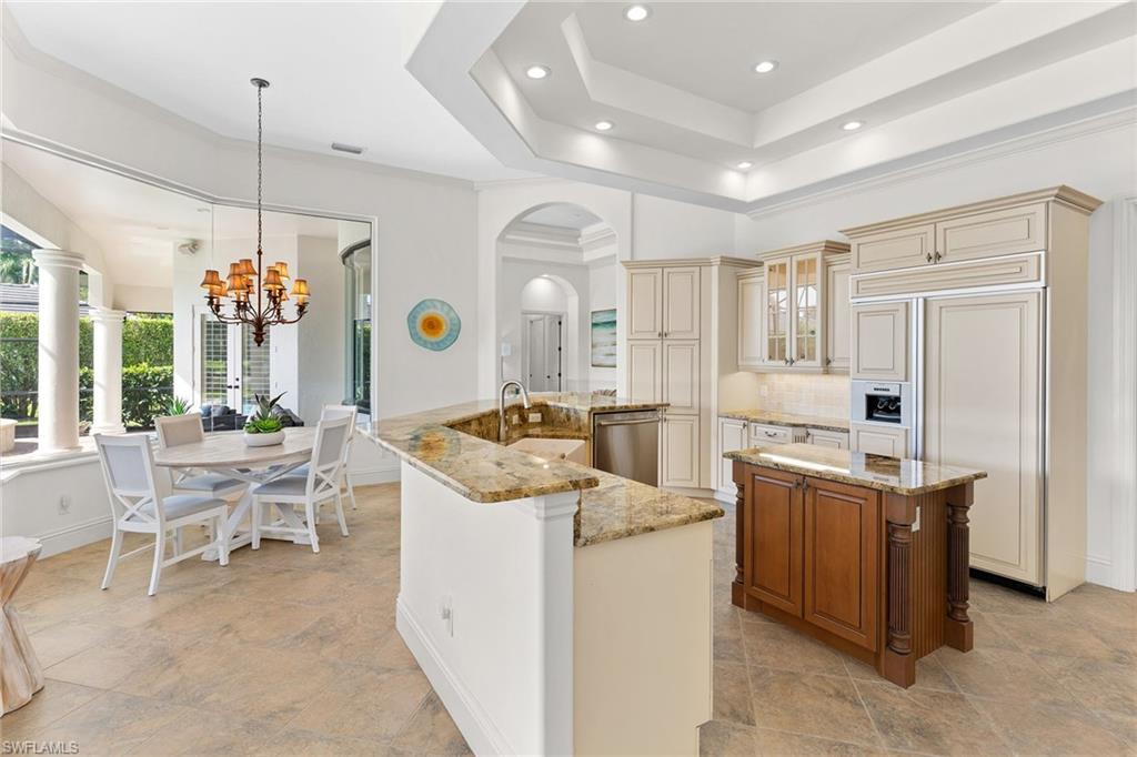 7506 Hogan Court Naples, FL 34113 - Photo 36 of 49 Kitchen with paneled built in fridge, light stone countertops, arched walkways, a chandelier, and dual tone cabinets