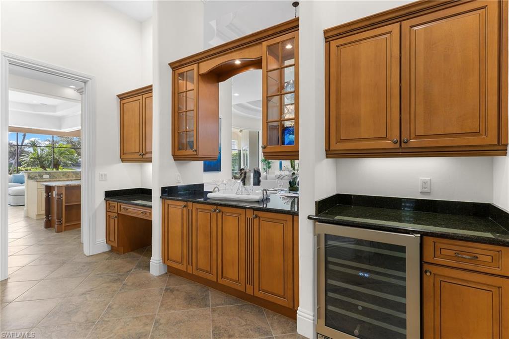 7506 Hogan Court Naples, FL 34113 - Photo 37 of 49 Bar area with wood finish cabinetry, wine cooler, glass insert cabinets, dark stone countertops, and healthy amount of natural light